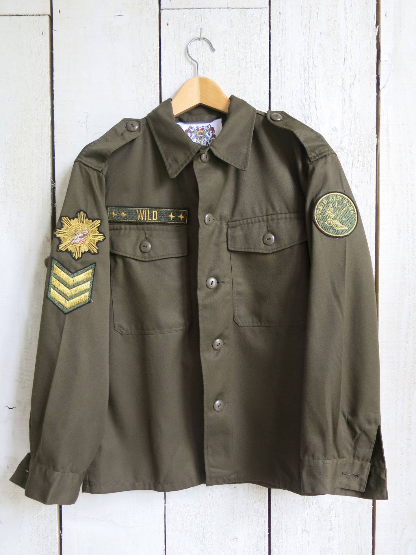 Olive green military jacket with decorative patches and "WILD" chest embroidery, front view.